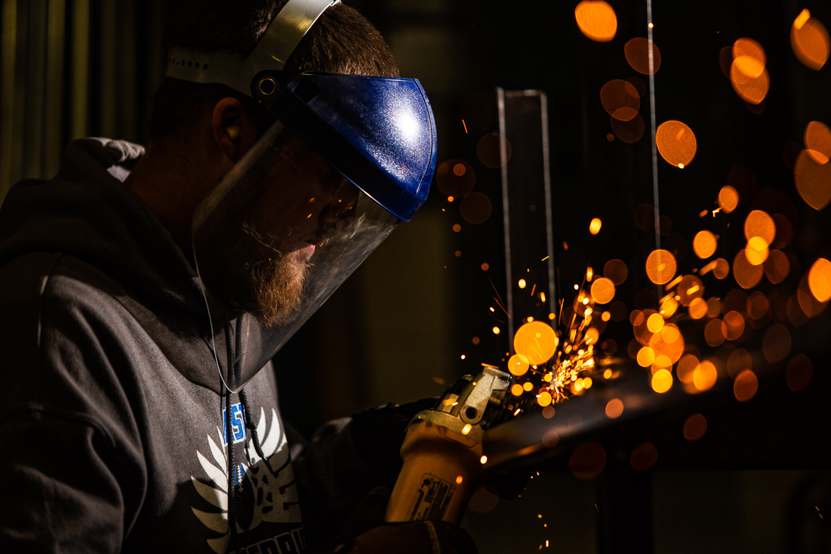 High school senior boy welding with orange sparks coming of the medal