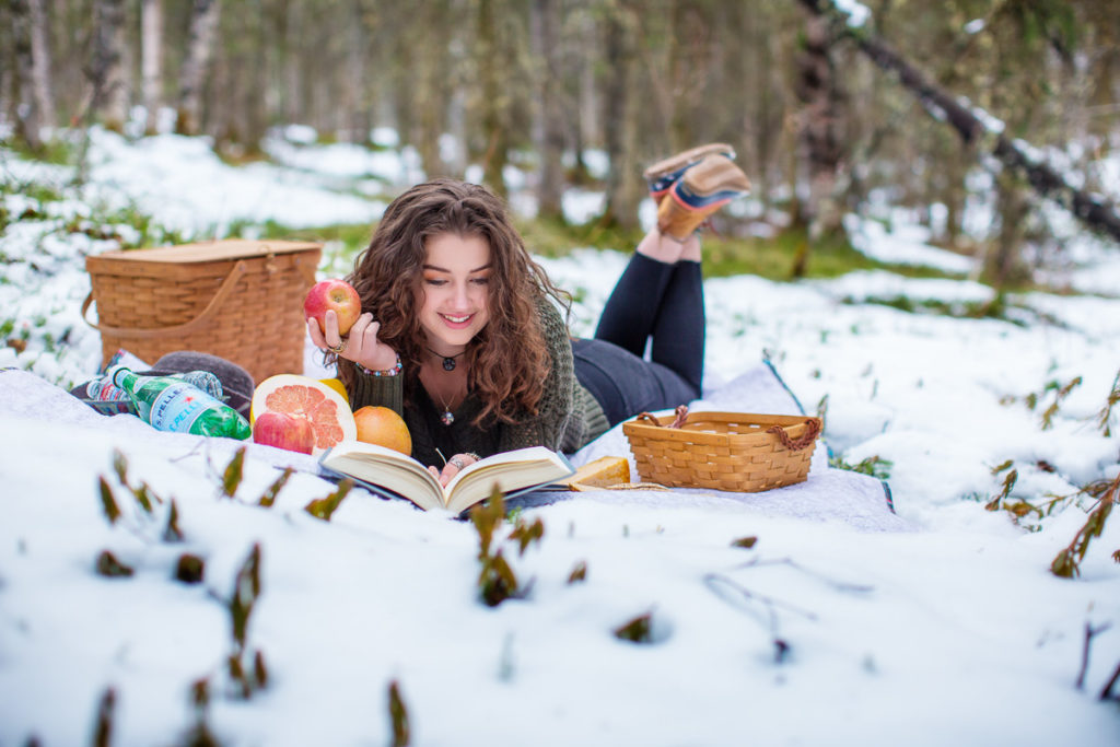 High school senior girl having a picnic in the snow while reading a book
