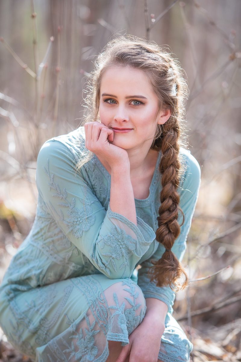 High school senior girl sitting in the woods wearing a blue dress