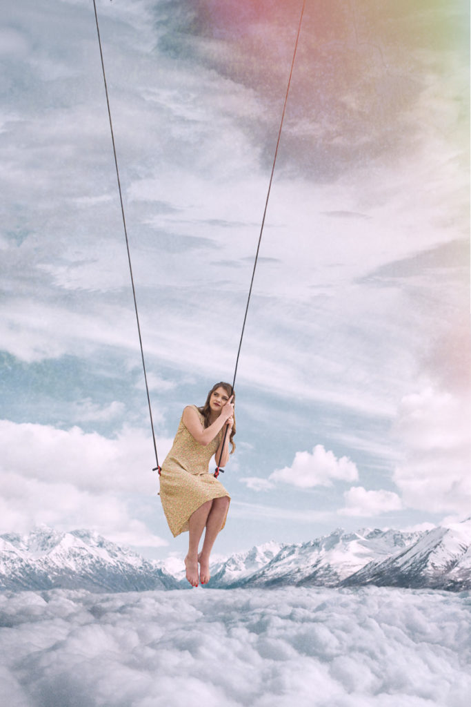 High school senior girl sitting on a swing above the clouds