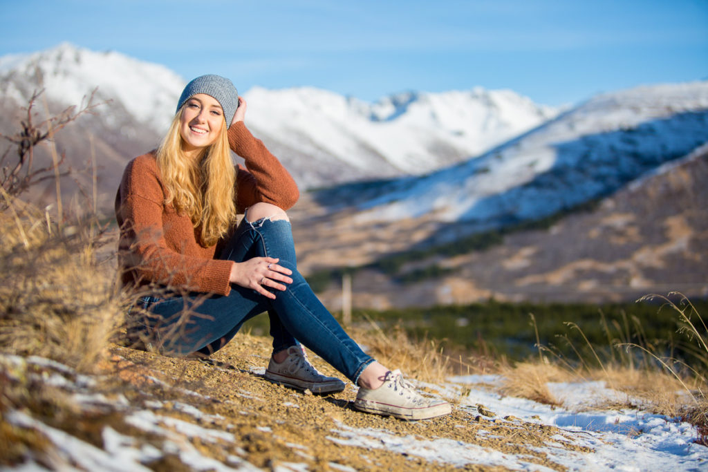 High school senior girl sitting in a field with mountains in the background