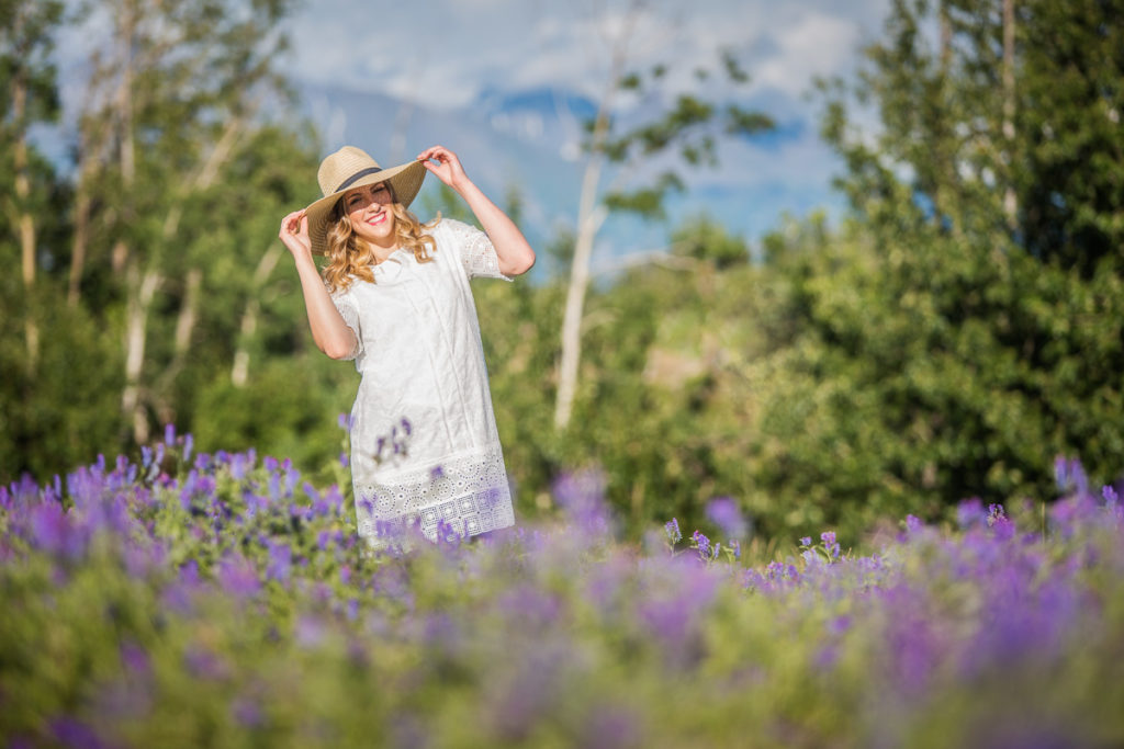High school senior girl standing ina field of purple flowers wearing a sun hat