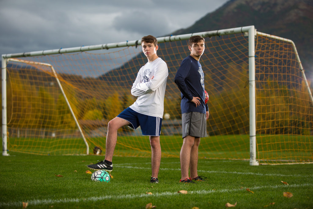 High school senior boys standing in front of a soccer goal, both are holding a soccer ball.