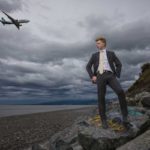 Hiram Kern-6665-1200x800 boy standing on a rock by the water with a plane going overhead