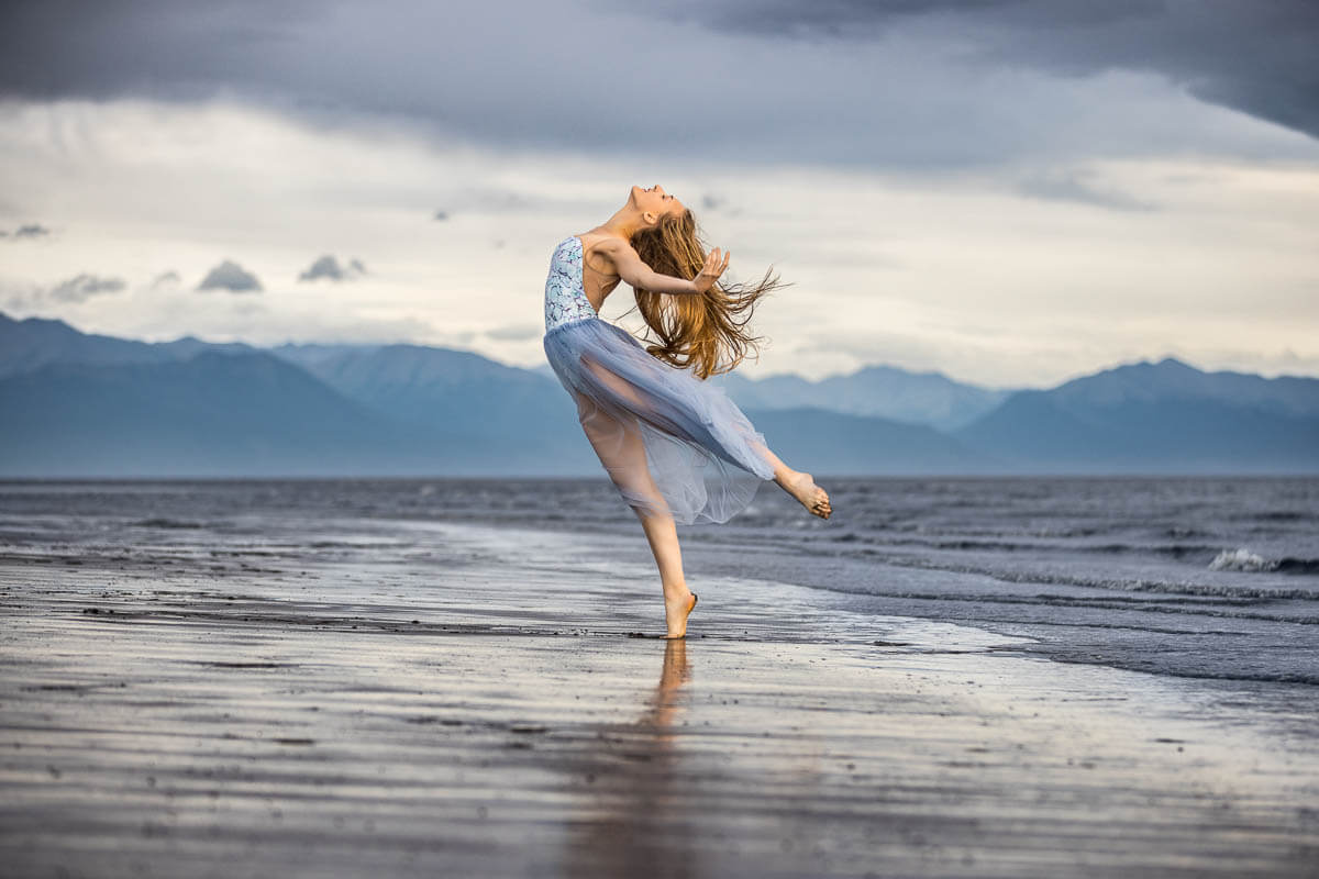 Grace dancer with long hair in arched arabesque on a windy beach