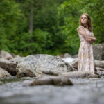 Brooke-Robertson-5718-copy girl standing in the river with rocks around her and trees behind her
