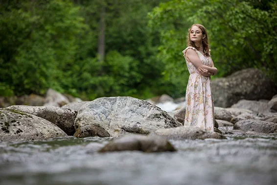 Brooke-Robertson-5718-copy girl standing in the river with rocks around her and trees behind her