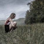 Ellie Rauckhorst-1293 girl scrunched down in a field of grass while in pointe shoes