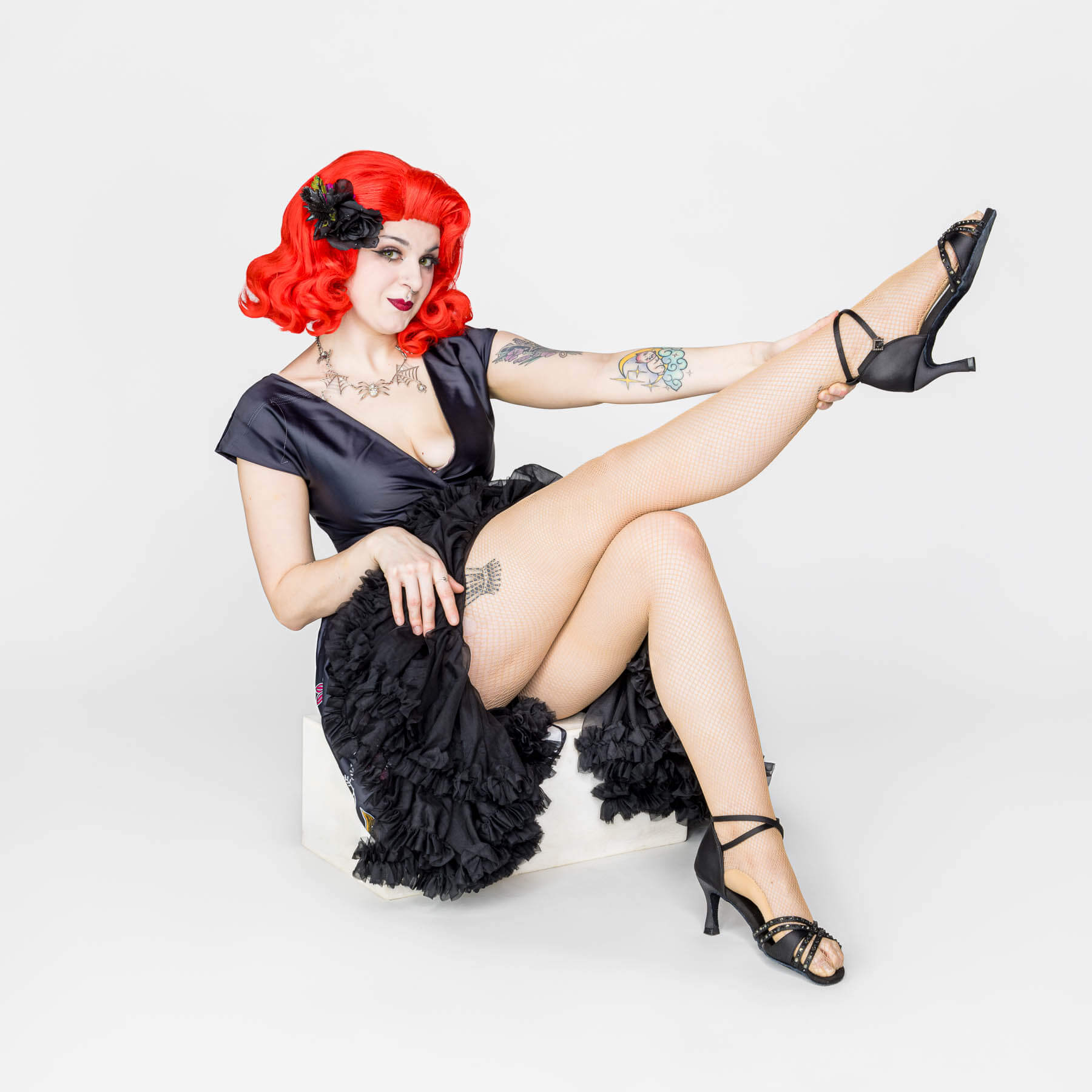 Pinup style photo of woman with pink hair sitting on a white box