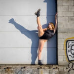 Greta-5530-copy girl in a black leotard and boots standing in front of a garage door
