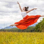 Lydia-Switzer-2012-copy girl in a long orange skirt leaping in a grassy field