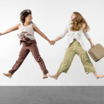 MDC-On My Way-0930 two women jumping while one of them holds a suitcase