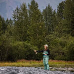 Megan-Traxinger-Concept-5840-min-copy girl standing in the water while fishing with trees and a moutain behind