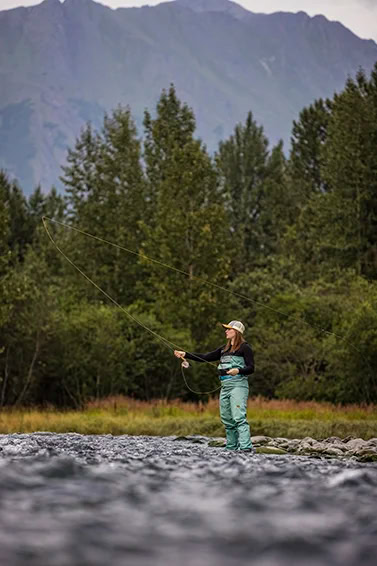 Megan-Traxinger-Concept-5840-min-copy girl standing in the water while fishing with trees and a moutain behind