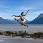 Sofia-Hernandez-Leon-3654-copy girl leaping over the sand with, rocks, water, and mountains behind