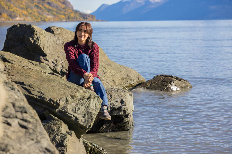 senior photos of a girl sitting on rocks by the water