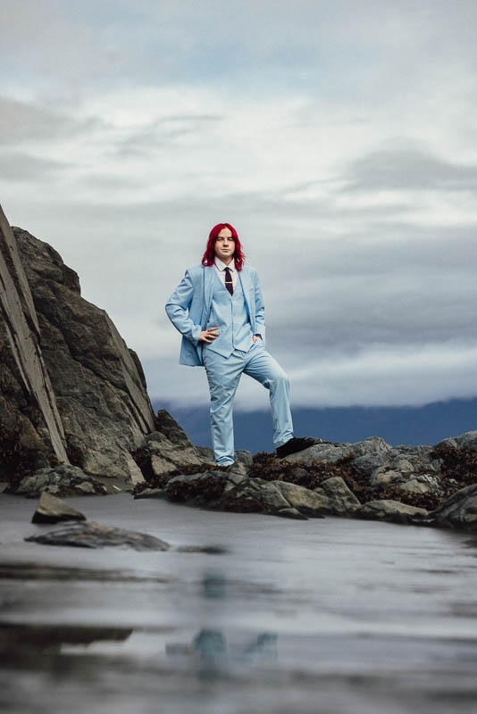 Senior photo of a high school boy with foot up on a rock wearing a blue formal suit