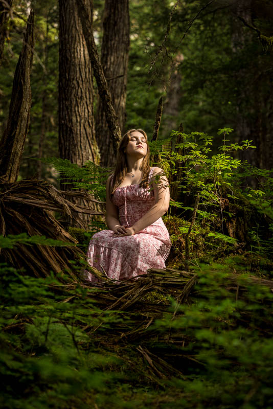 high school girl in a dress sitting in the forest looking up with eyes closed