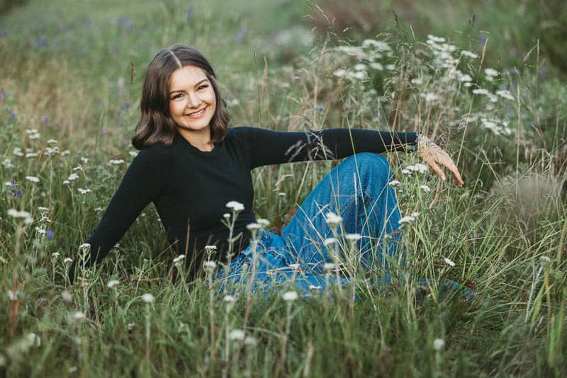 senior photos of a girl wearing a black long sleeve shirt and blue jeans sitting in the grass