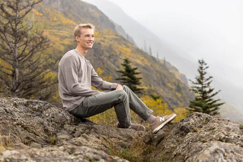 senior photos of a boy sitting rocks with moutains and trees behind
