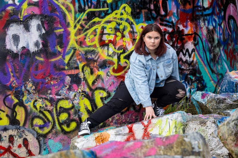 senior photo of a high school girl posing in front of a wall of graffiti