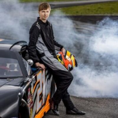 High school boy leaning on his race car holding a helmet