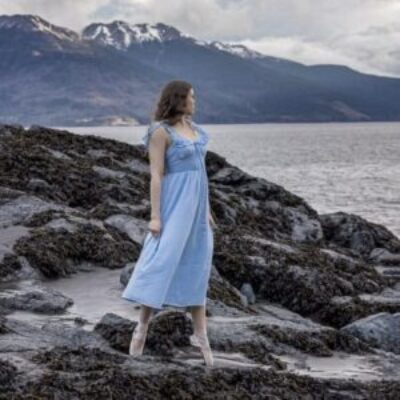 cloudy weather photo of a high school girl in a blue dress and point shoes standing on the rocks