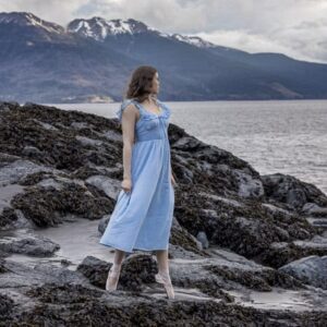 cloudy weather photo of a high school girl in a blue dress and point shoes standing on the rocks