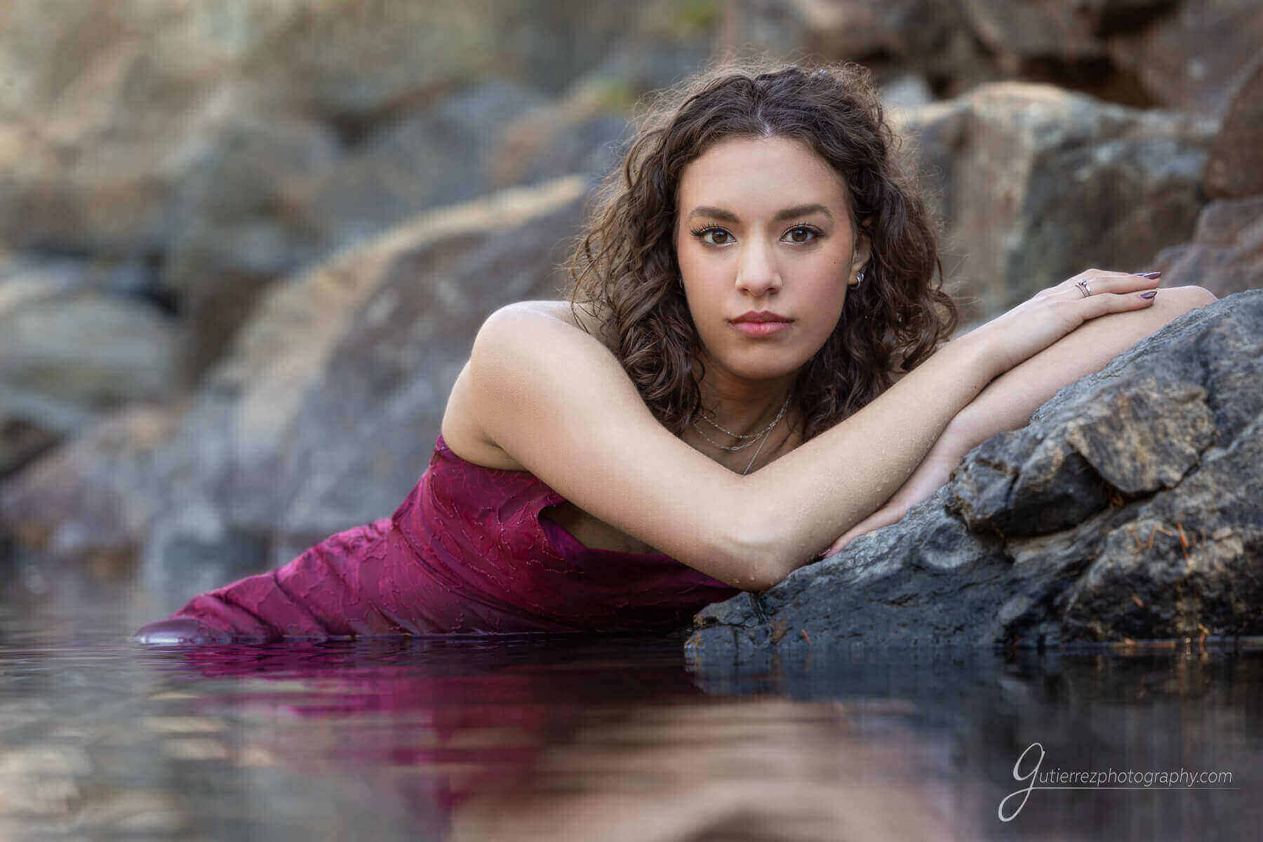 High school girl reclining in the water of a pond in a red dress