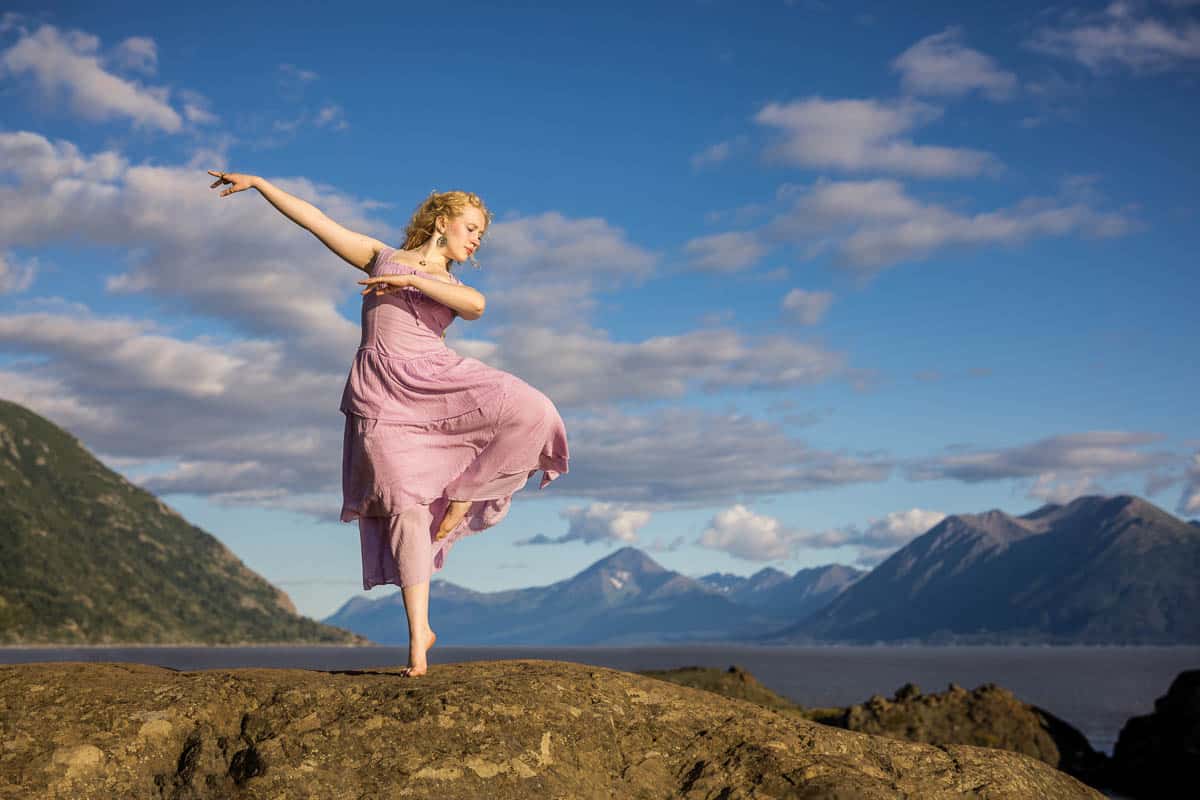 High school senior girl in a pink dress dance on rocks by coast