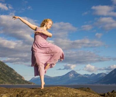 High school senior girl in a pink dress dance on rocks by coast
