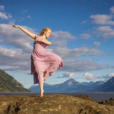 High school senior girl in a pink dress dance on rocks by coast